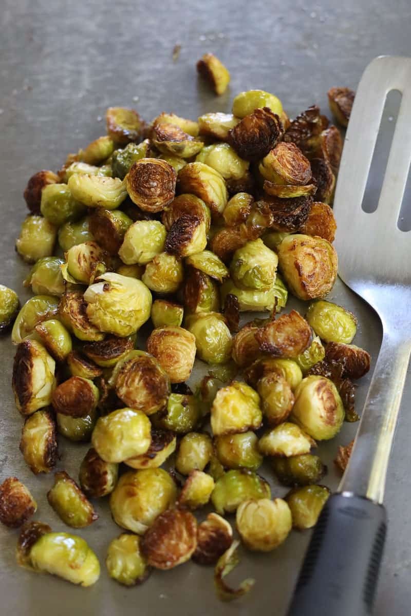 Roasted Brussels sprouts on a baking sheet next to spatula.