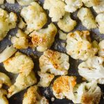 Roasted cauliflower on a baking sheet with sprinkled spices.