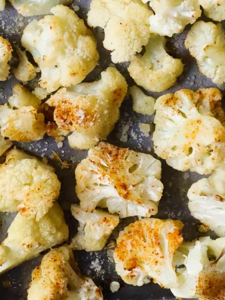 Roasted cauliflower on a baking sheet with sprinkled spices.
