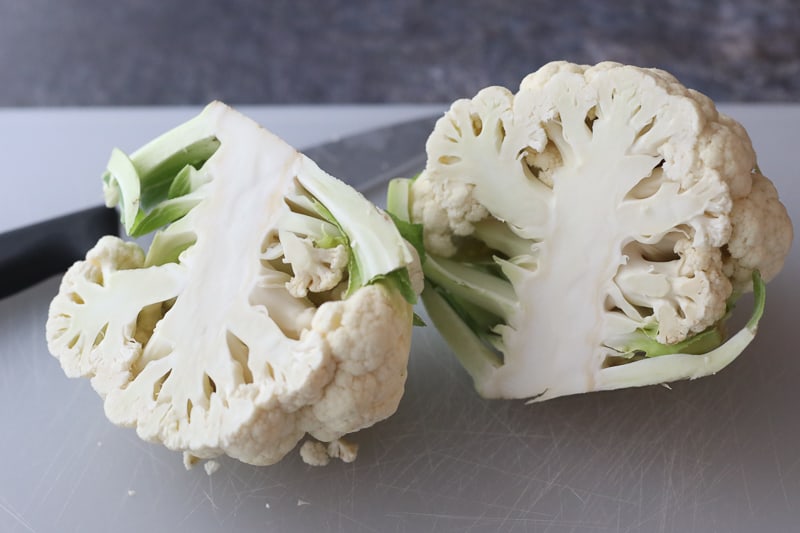 Cauliflower head sliced in half on white cutting board.