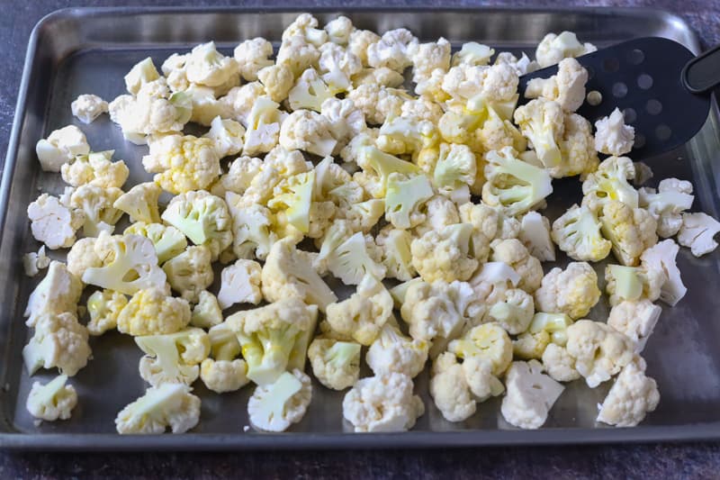 Cauliflower florets on sheet pan with black spatula tossing to coat with butter.