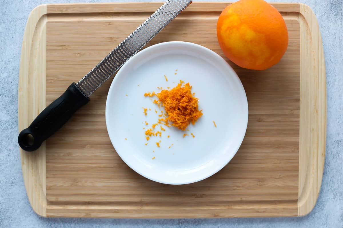 Grated orange peel on a small white plate next to a Microplane grater and a Navel orange.