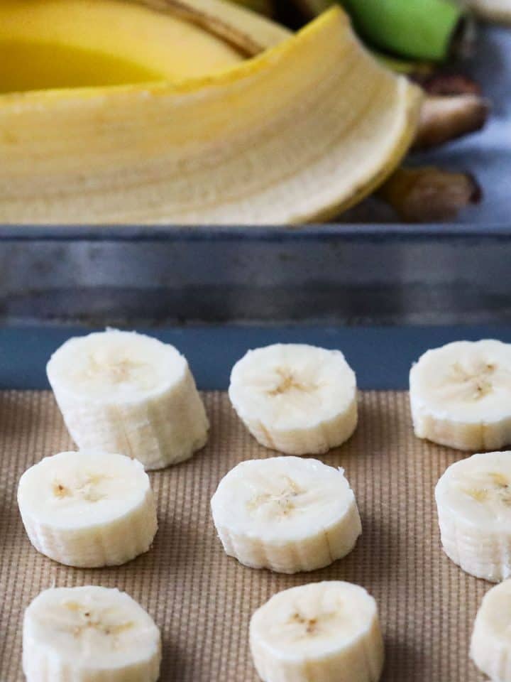 Sliced bananas on a baking sheet with banana peels on the side.