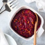 Homemade cranberry sauce in a white serving dish with a wooden spoon.