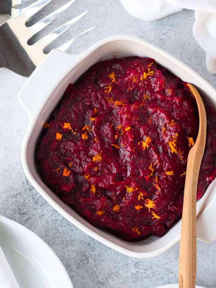 Homemade cranberry sauce in a white serving dish with a wooden spoon.