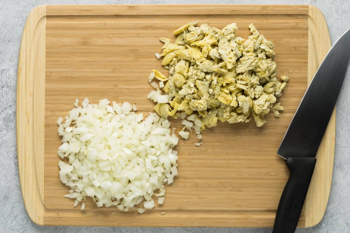 Chopped onions and artichokes on a cutting board with chef's knife.
