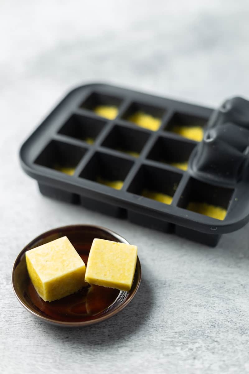 Frozen ginger paste cubes in a silicone ice cube tray with two popped out and placed on a small dish.