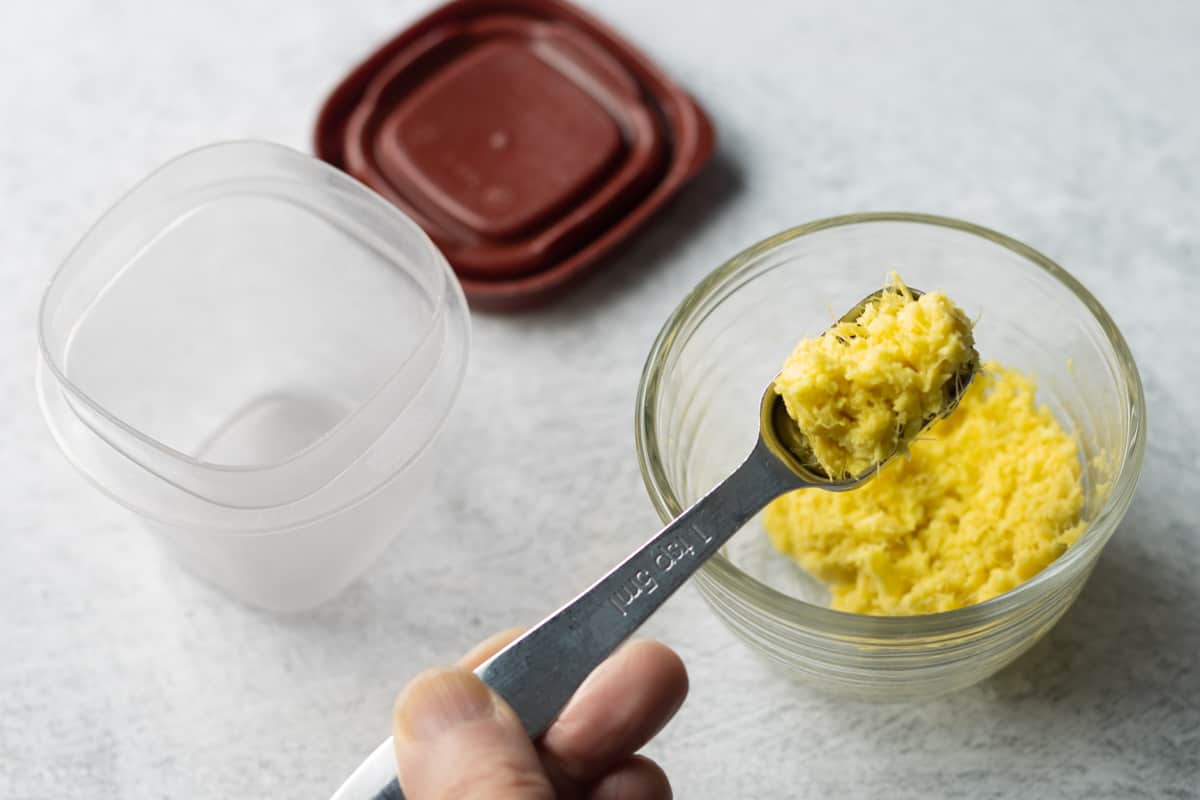 Frozen ginger paste slightly defrosted in a glass container with 1 teaspoon removed for use.