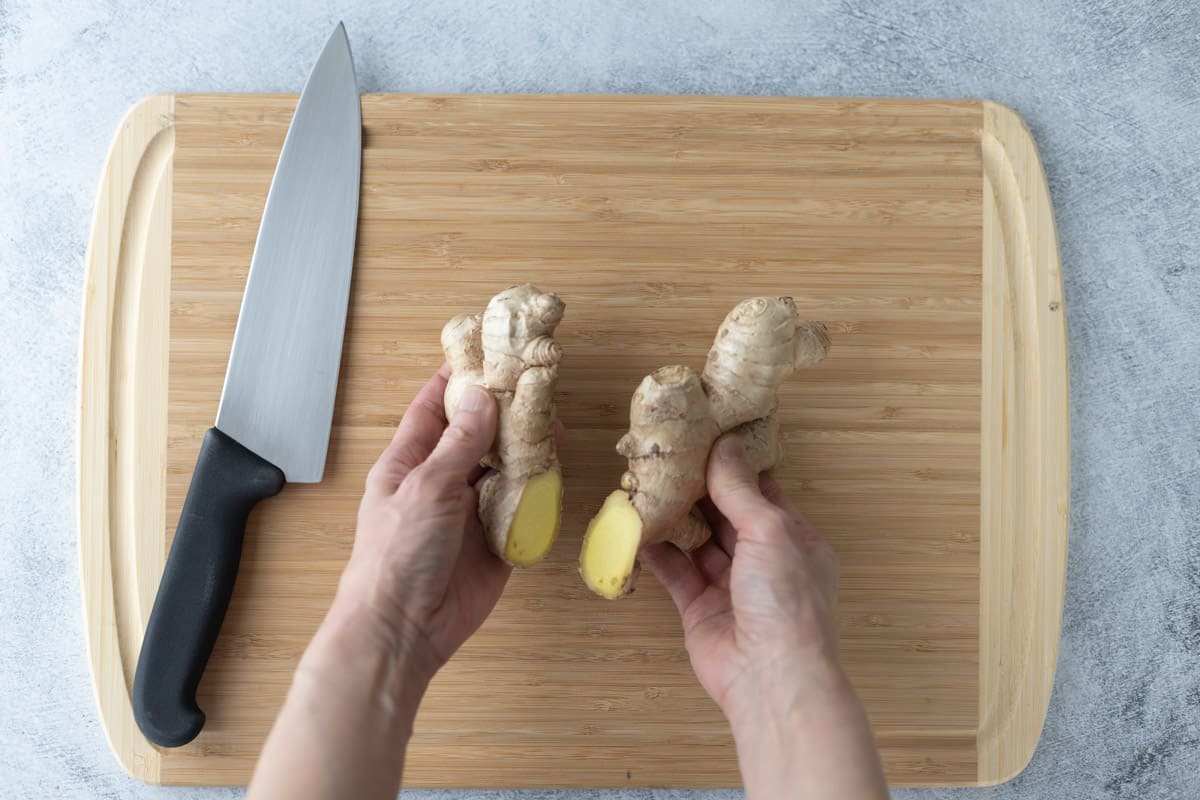 Whole ginger root cut in half using a chef's knife on a bamboo cutting board.