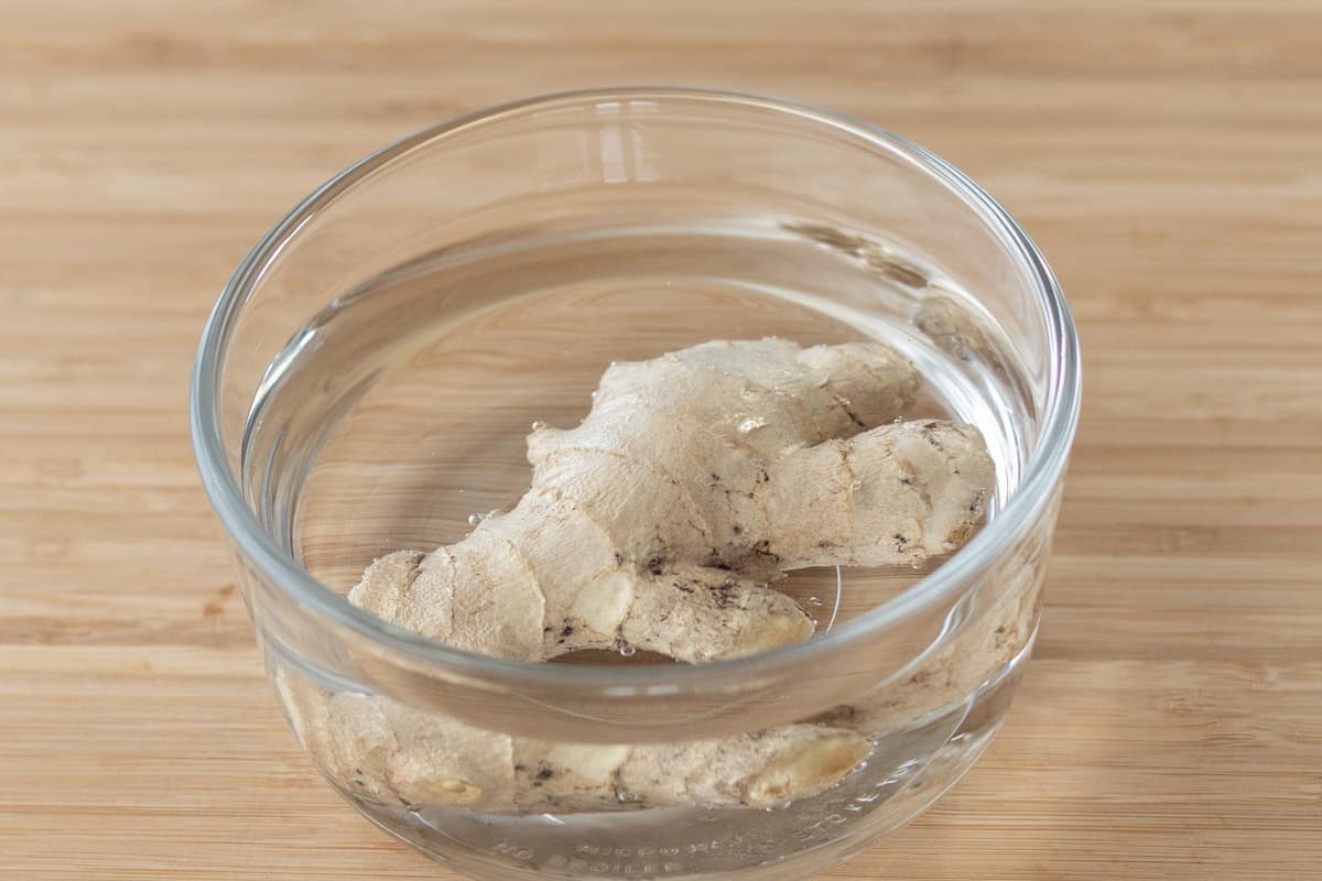 Whole ginger root soaking in water inside a glass container.