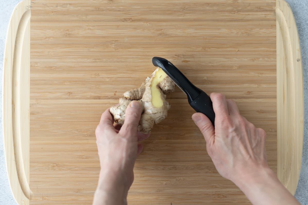 Ginger root being peeled using a vegetable peeler.