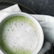 Matcha latte in a white mug resting on a white napkin on a dark gray background.