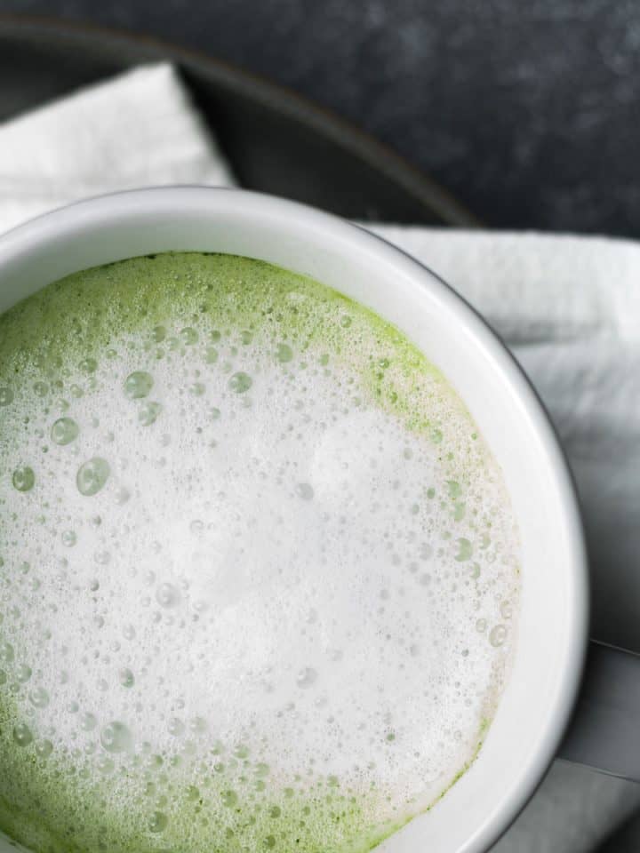 Matcha latte in a white mug resting on a white napkin on a dark gray background.