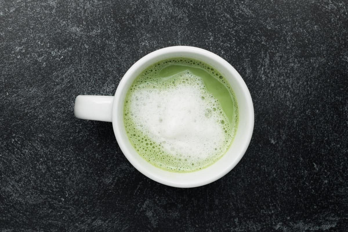 A top-down view of a mug of vanilla matcha tea with frothed milk.