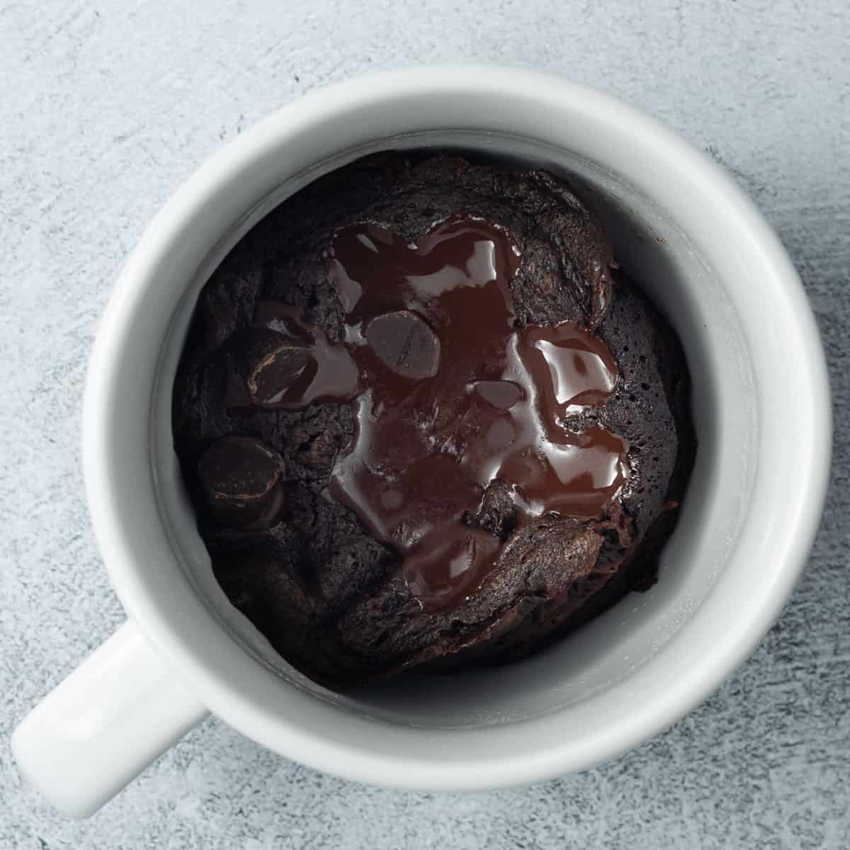 Top-down view of a chocolate protein powder mug cake with chocolate chips in a white mug.