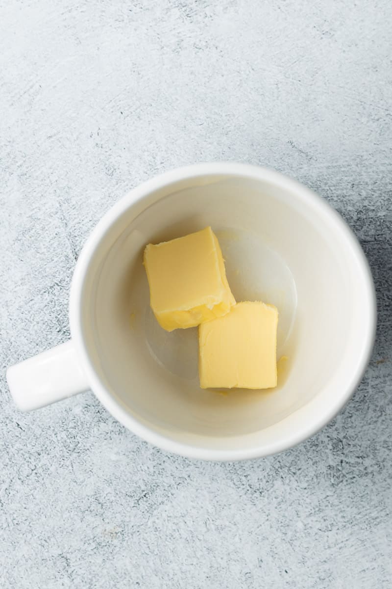 Two cubes of solid butter inside a white mug.