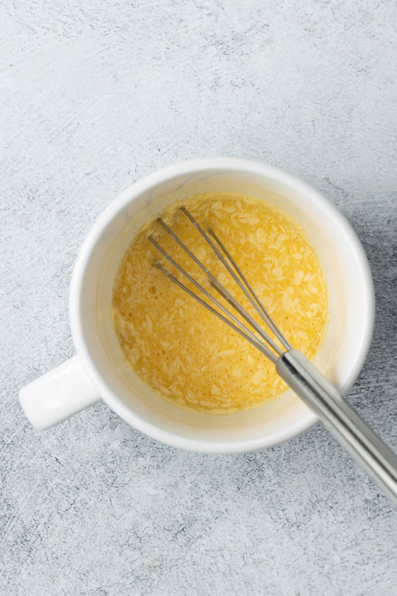 Softened butter and raw egg combined in a white mug with a metal whisk in the mug.