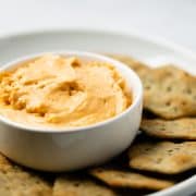 Flourless cheese sauce in a white bowl surrounded by a plate of crackers.
