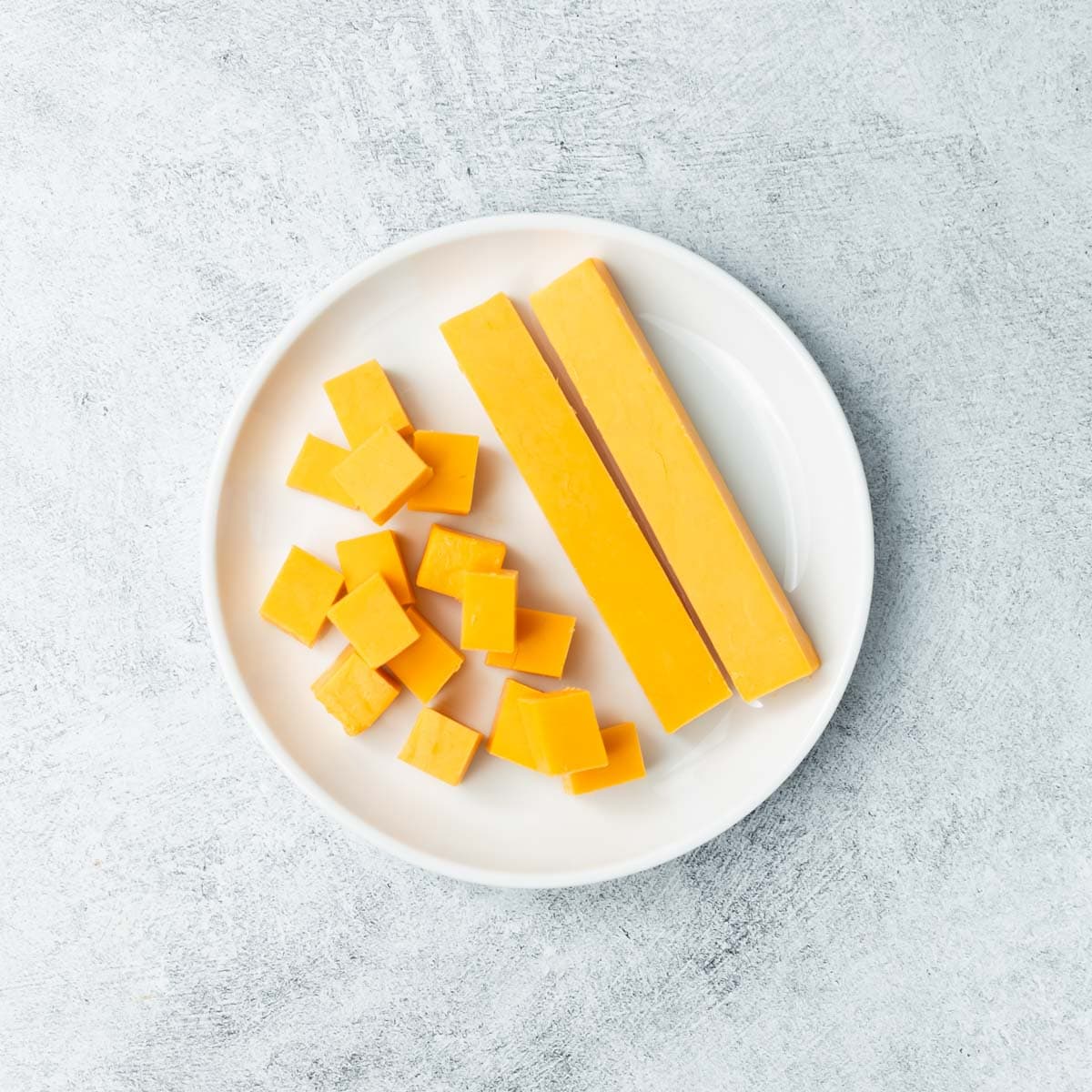 Cubed cheese and 2 cheese strips on a white plate.