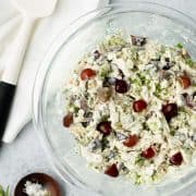 Chicken salad in a glass mixing bowl with a white spatula and a wooden bowl of salt and pepper on the side.