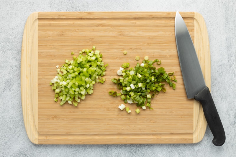 Bamboo cutting board with diced celery, diced green onions and chef's knife.