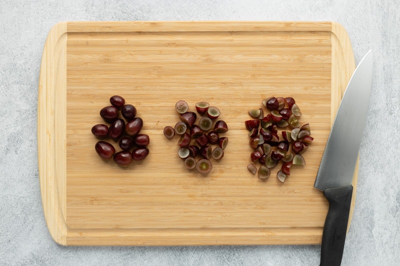 Bamboo cutting board with whole, halved, and quartered red seedless grapes and chef's knife.