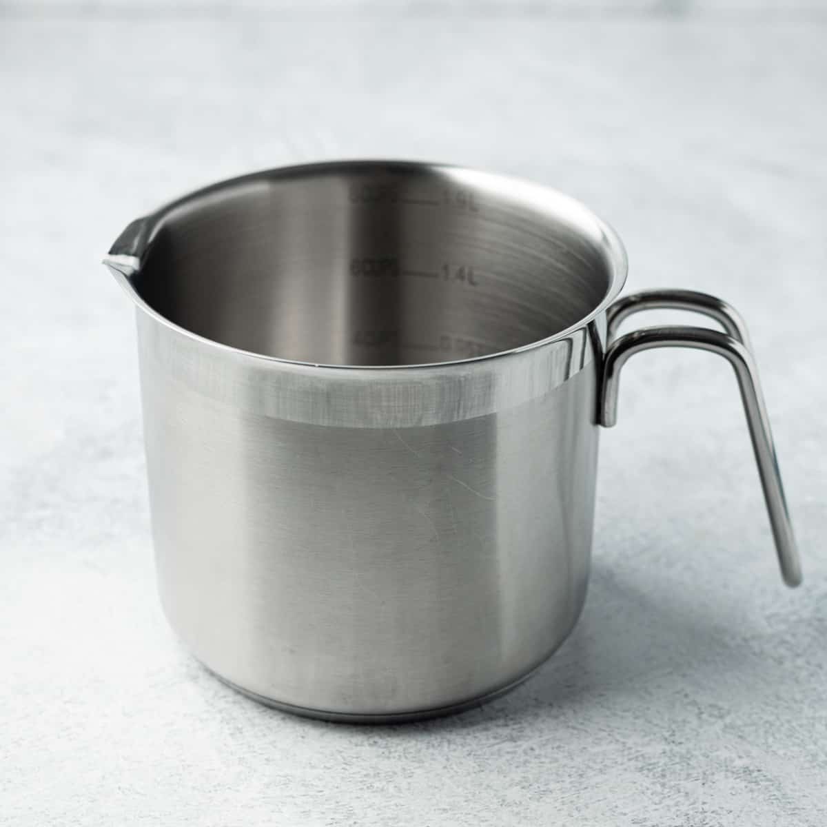 Small stainless-steel pot with a curved handle that contains interior measurements in cups and liter units.
