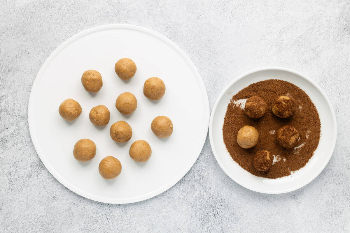 Snickerdoodle cookie dough divided into 16 balls on a white plate, next to another white plate with cookie balls rolled in cinnamon sugar coating.
