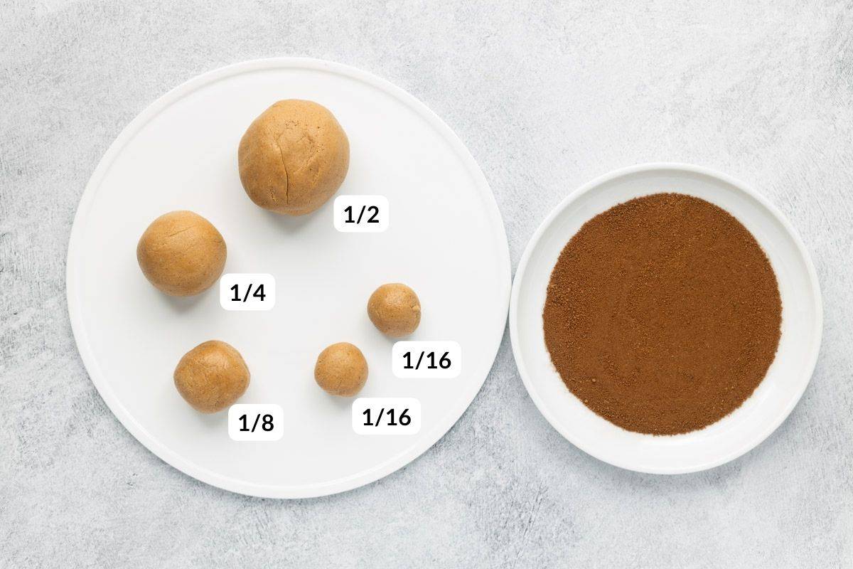 Cookie dough divided 4 times with labels showing ½, ¼, ⅛, and 1/16 portions on a white plate, next to another plate with a mix of coconut sugar and cinnamon.