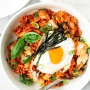 Kimchi fried rice with chicken and a sunny-side-up fried egg in a white bowl with a spoon.