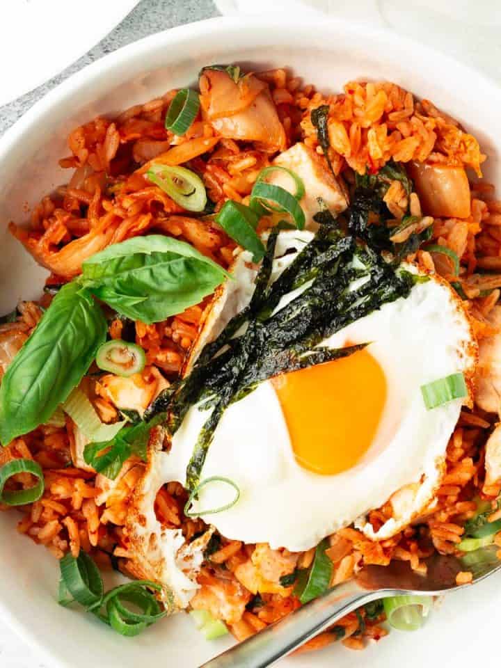 Kimchi fried rice with chicken and a sunny-side-up fried egg in a white bowl with a spoon.