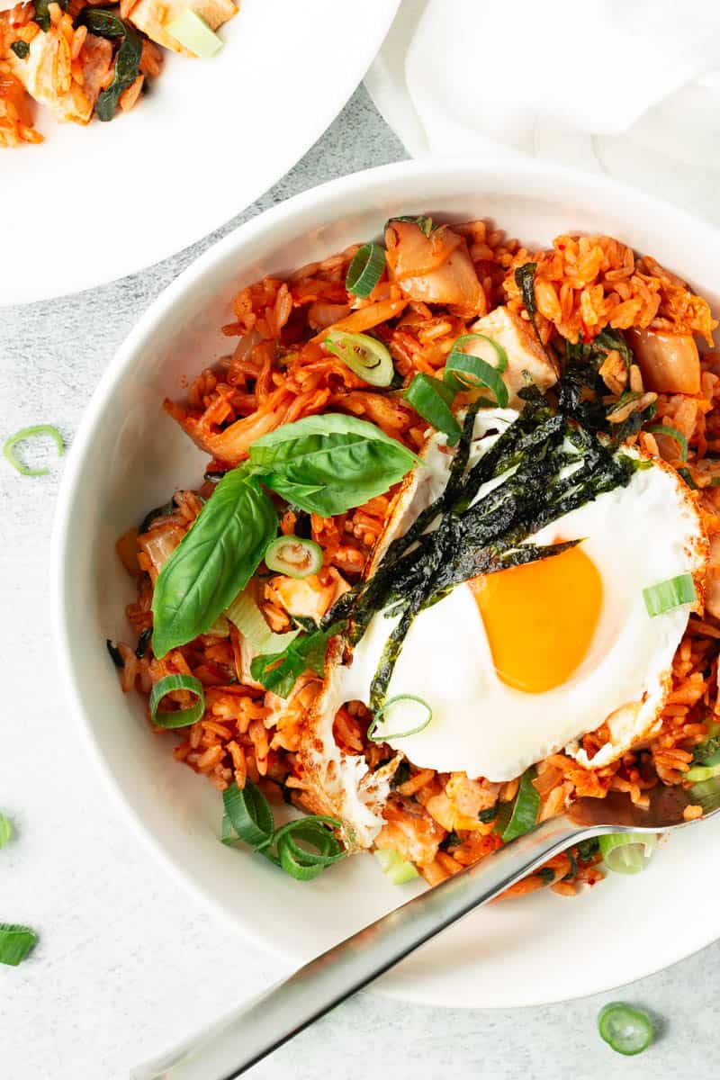 Kimchi fried rice with chicken and a sunny-side-up fried egg in a white bowl with a spoon.