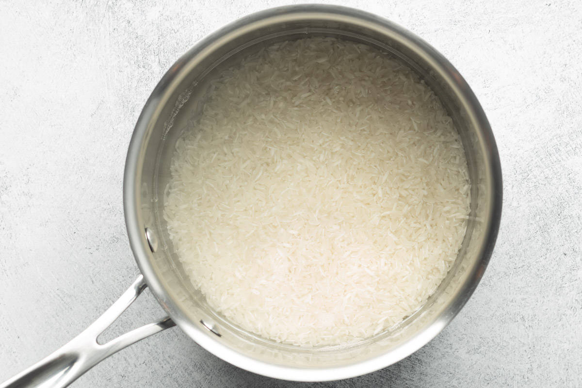 Jasmine rice and water added to a medium-sized stainless-steel pot for cooking.