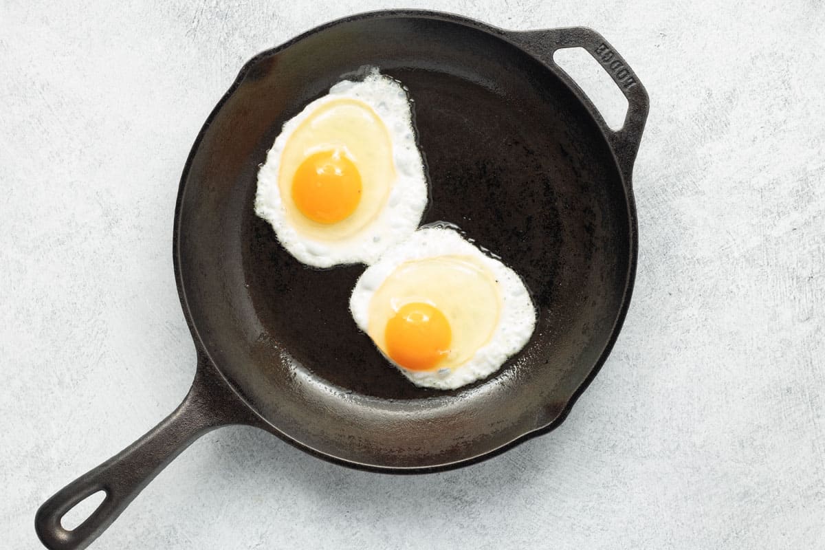 Two cracked eggs added to a smaller cast-iron skillet.