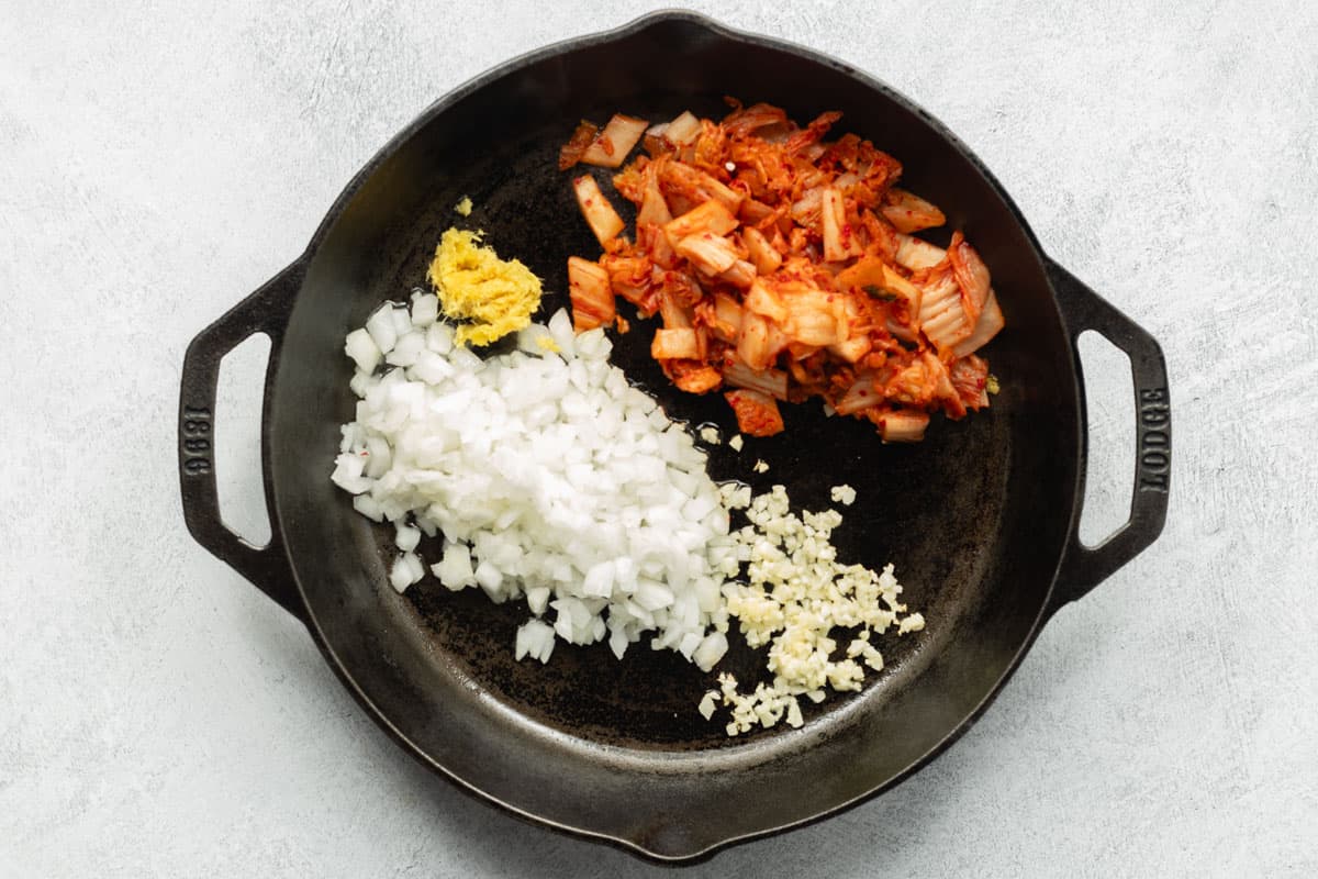 Chopped onion, kimchi, garlic, and ginger added to a heated cast-iron skillet.