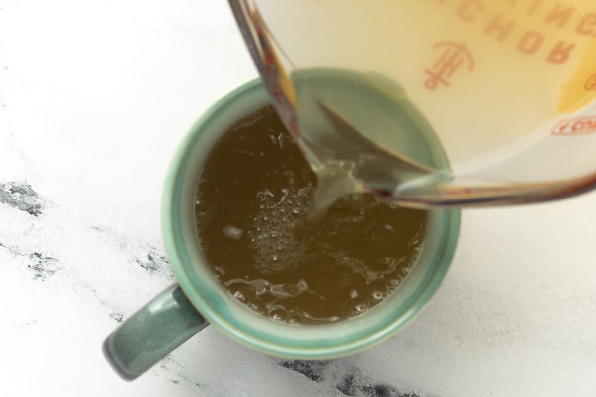 Lemongrass ginger tea is being poured into a mug.
