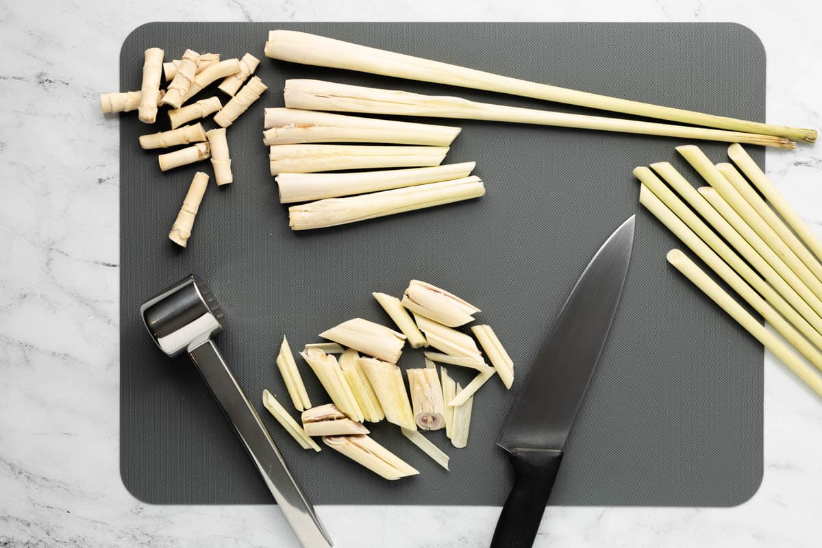 Lemongrass on a gray cutting board with stems and the top halves removed, while the remaining pieces are sliced and mashed.