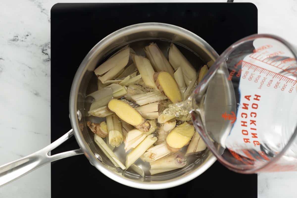 Water is being added to the chopped lemongrass and sliced ginger in a medium saucepan.
