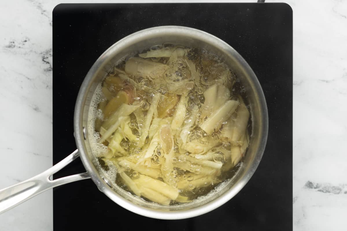 Lemongrass, ginger, and water are boiling in a medium saucepan.