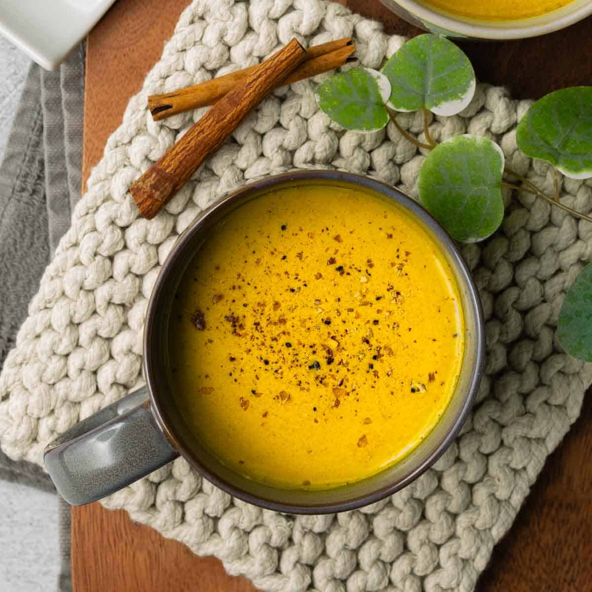 Top-down view of a gray mug of golden milk resting on a light gray rope trivet with a walnut wood tray underneath.