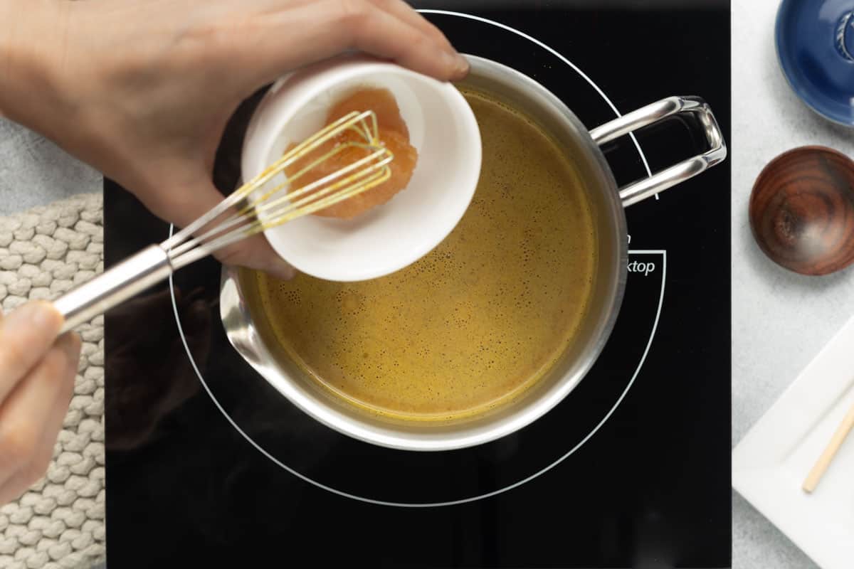 Honey is being added to the golden milk that is simmering over the stove.