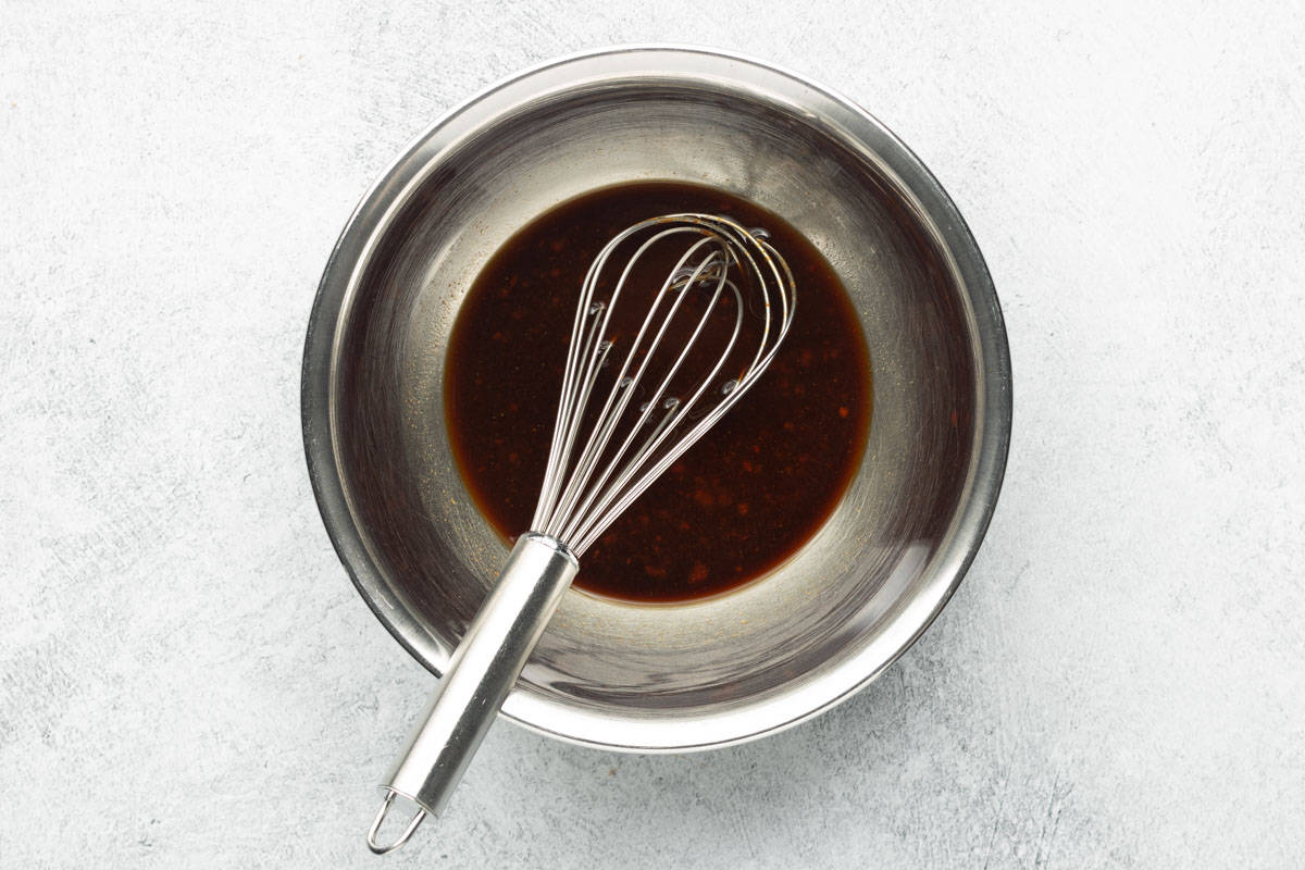 Sauce ingredients are combined in a stainless-steel bowl with a balloon whisk.