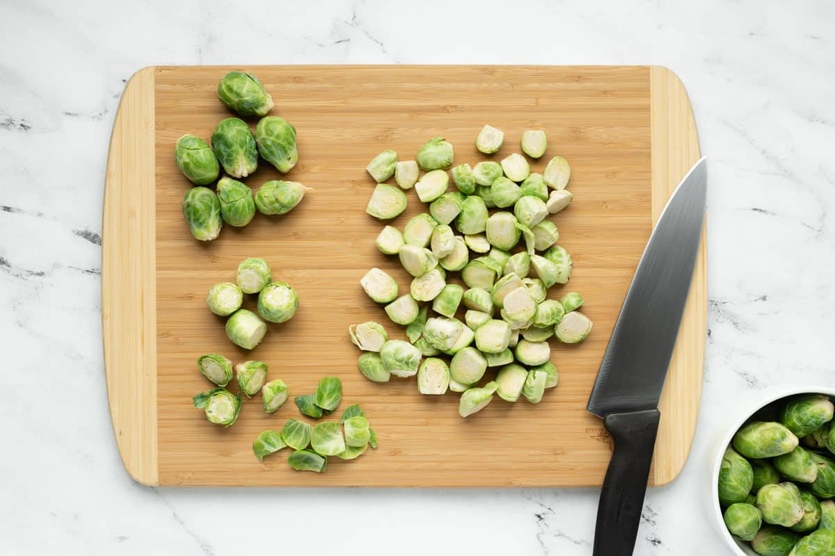 Brussels sprouts sliced in half with stems and outer leaves removed, on a bamboo cutting board.