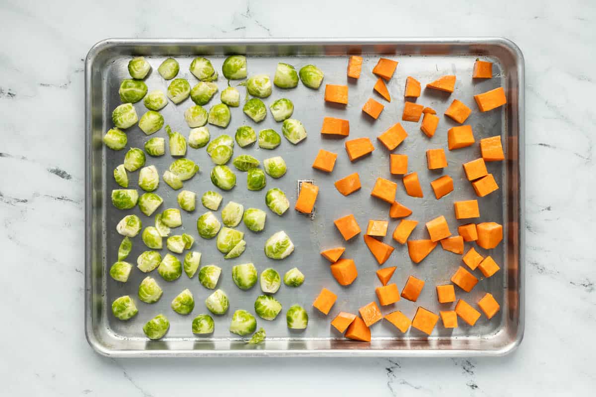 Baking sheet filled with half Brussels sprouts and half cubed sweet potatoes.