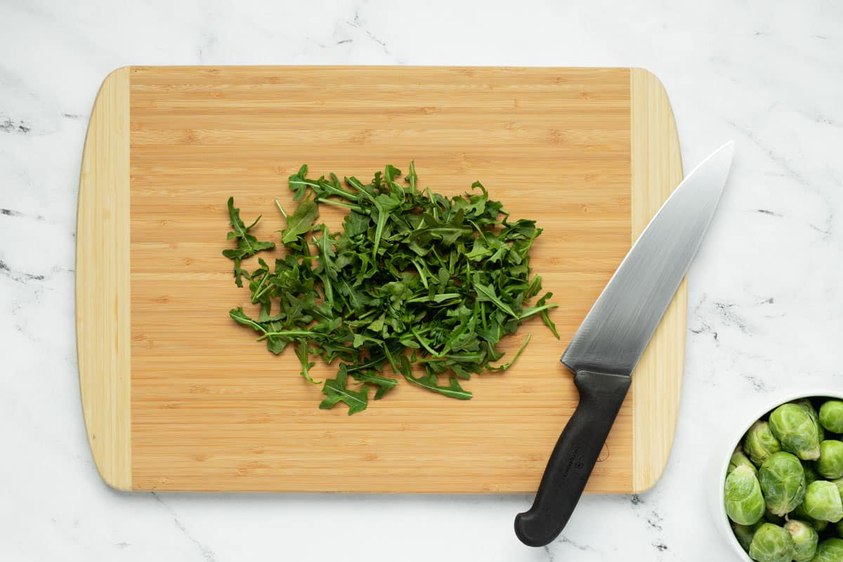 Chopped arugula resting on a bamboo cutting board with chef's knife.