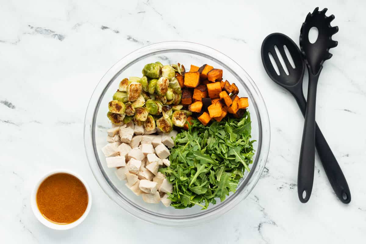 Curry chicken salad with roasted vegetables in a glass mixing bowl, not yet combined with the curry salad dressing.