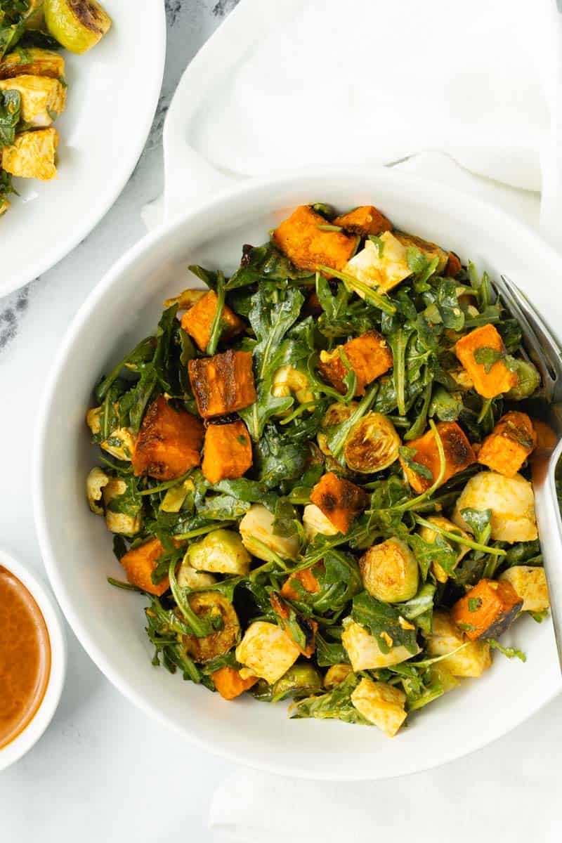 Curry chicken salad with roasted vegetables in a white bowl, next to a small bowl of extra dressing.