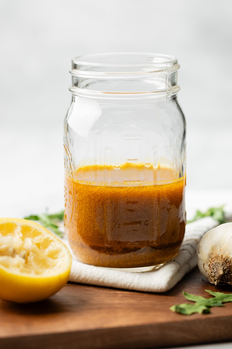 Curry salad dressing in a mason jar with a juiced lemon and garlic on the side.