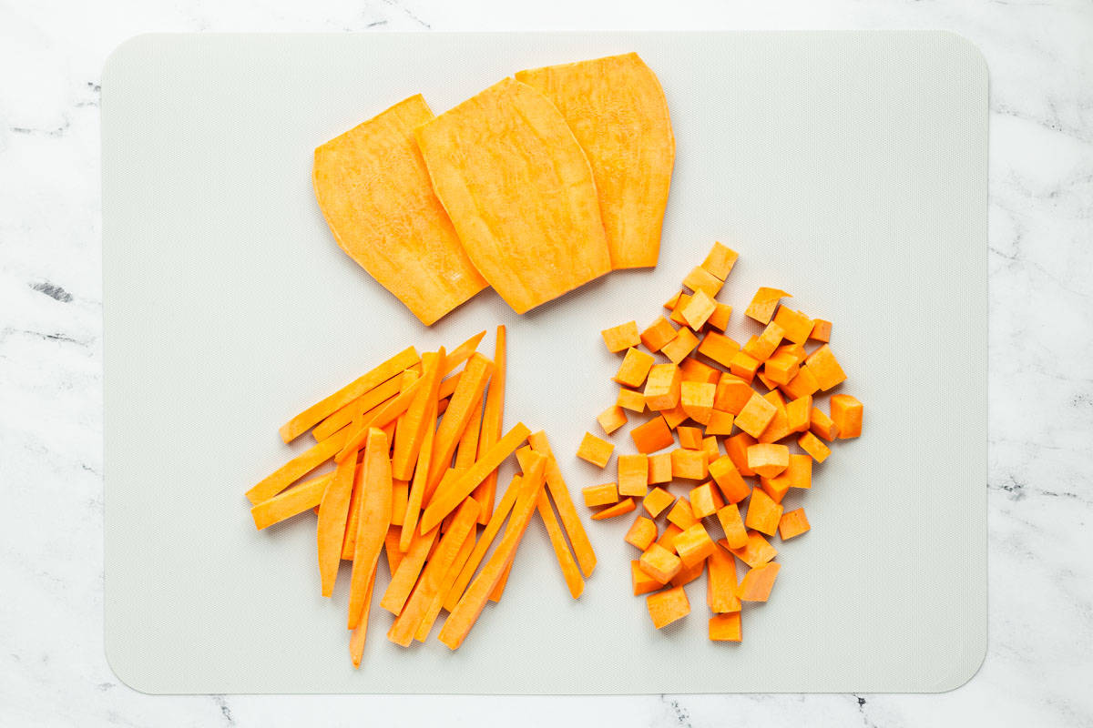 Sliced, cubed, and slivered sweet potatoes are laid out on a light grey cutting board after 6 days of storage in the refrigerator.