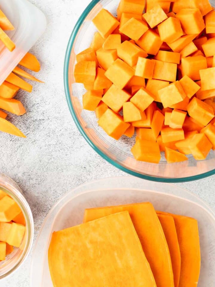 Sliced, cubed, and cut sweet potatoes are in separate storage containers on a textured grey counter.